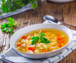 Chicken broth. Bone broth with noodles carrot and parsley in white bowl.