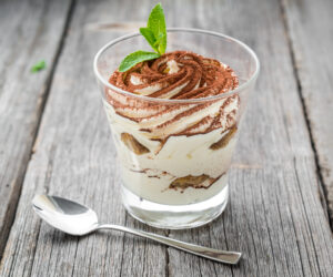 Traditional Italian dessert tiramisu in a glass. On a wooden table