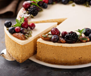 Pumpkin cheesecake with sour cream topping and fresh seasonal berries and nuts with a slice taken out