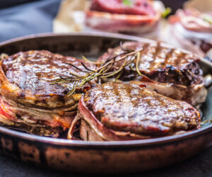 Three grilled beef tenderloin steaks coated bacon on a frying pan.