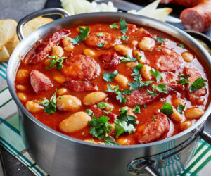 hearty beans stew with sausages, herbs and spices in tomato sauce in a metal casserole on a concrete table with ingredients, fasolka po bretonsku, polish cuisine, view from above,close-up