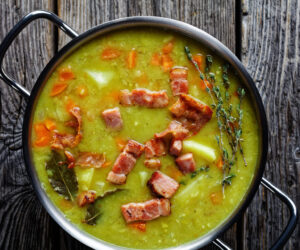 German one pot split pea soup erbseneintopf with bacon, pork meat, carrot, potato with thyme - winter comforting dish served on a pot on an old barn wooden table, horizontal orientation, close-up