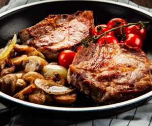 Pork steaks in frying pan with champignons, onion and tomatoes