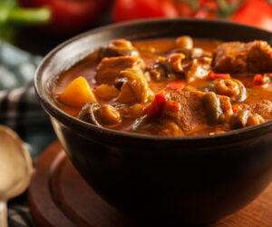 Stew soup with meat, potatoes, mushrooms and red pepper in bowl
