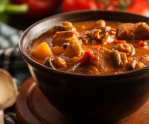 Stew soup with meat, potatoes, mushrooms and red pepper in bowl