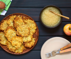 Homemade potato pancakes or fritters on wooden plate with apple sauce, a traditional dish in Germany, photographed overhead on dark wood with natural light
